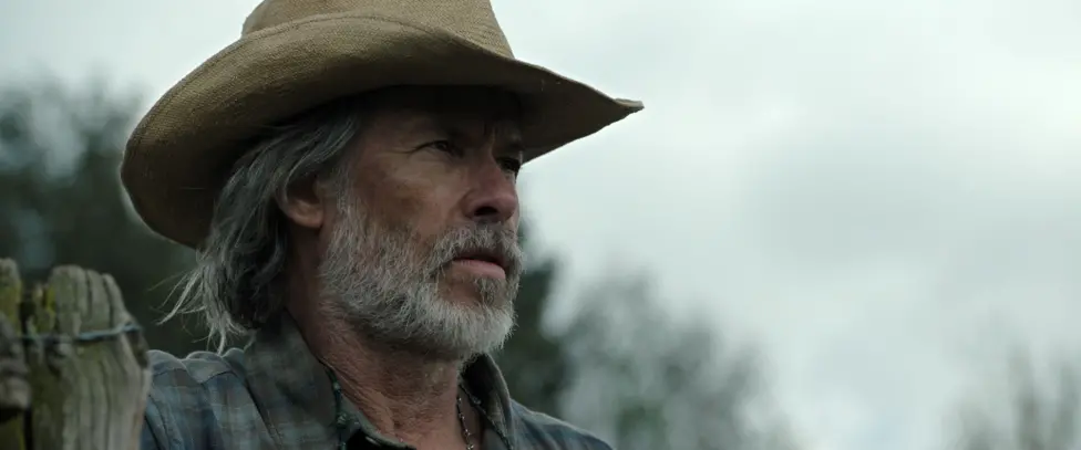 Still from The Dog Stars of Guy Pearce as Pops, wearing a beige cowboy hat and sporting an unkempt beard and hairstyle.