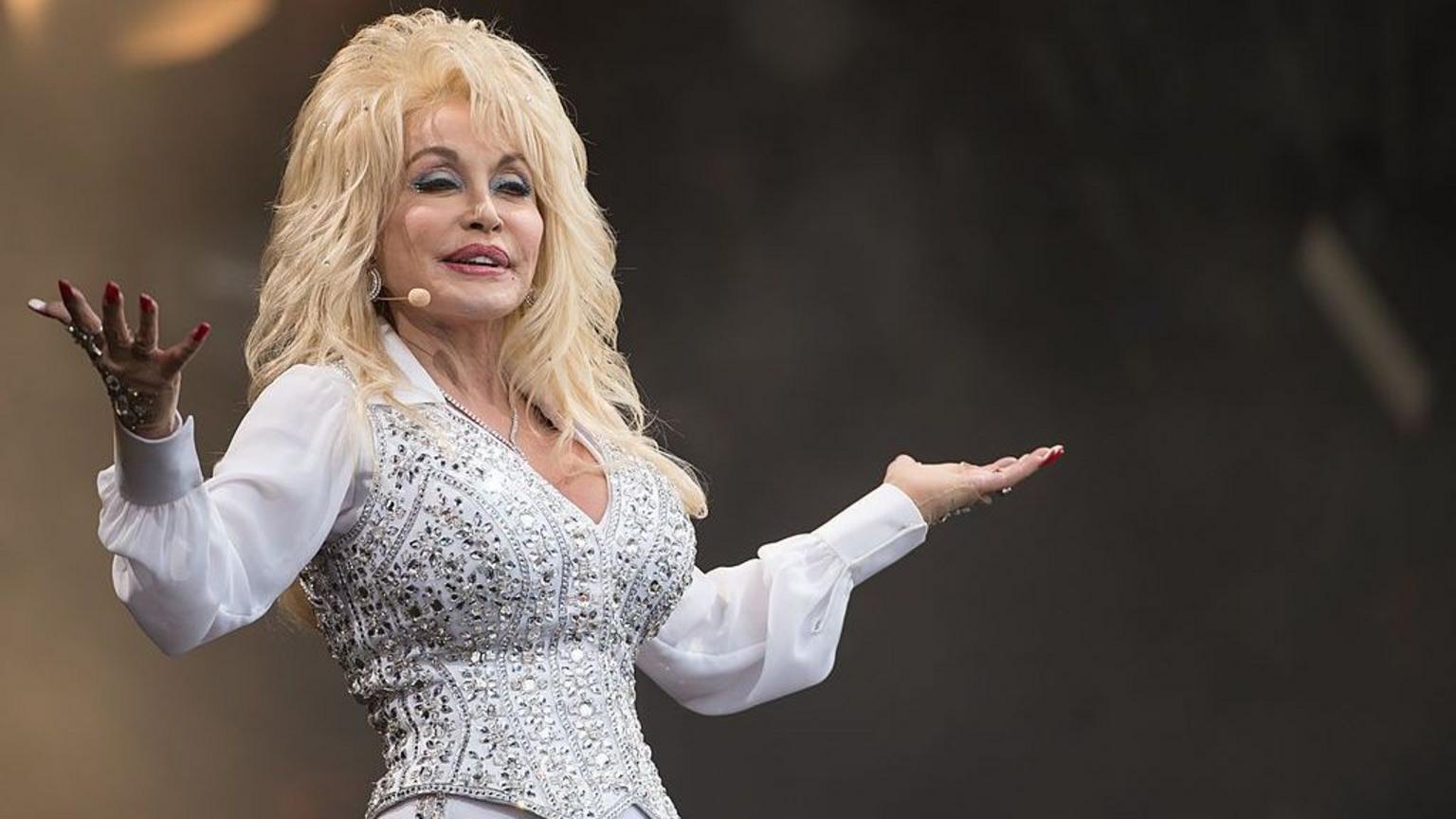 Dolly Parton smiling on a red carpet in a glittering outfit