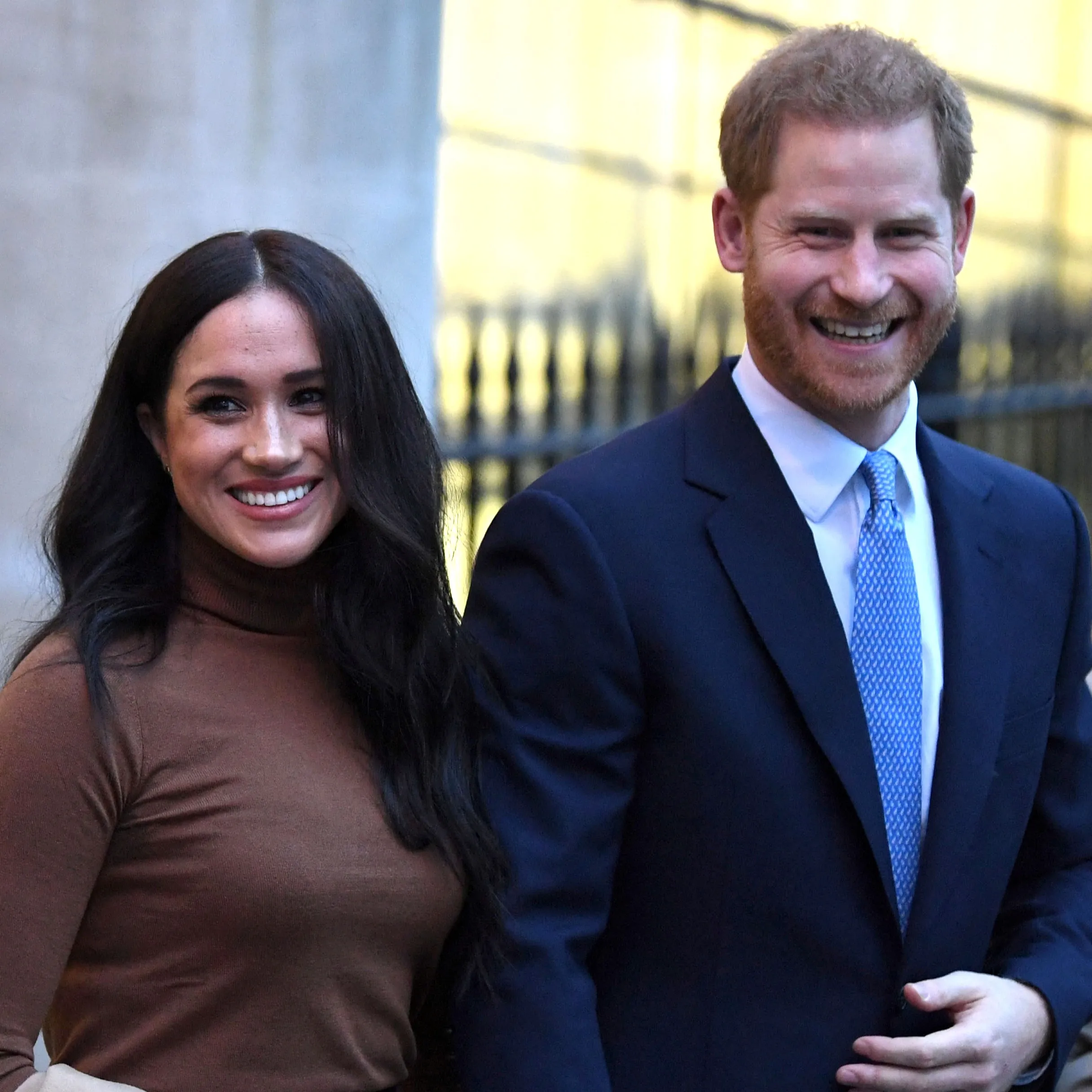 Meghan Markle and Prince Harry smiling and walking outdoors.