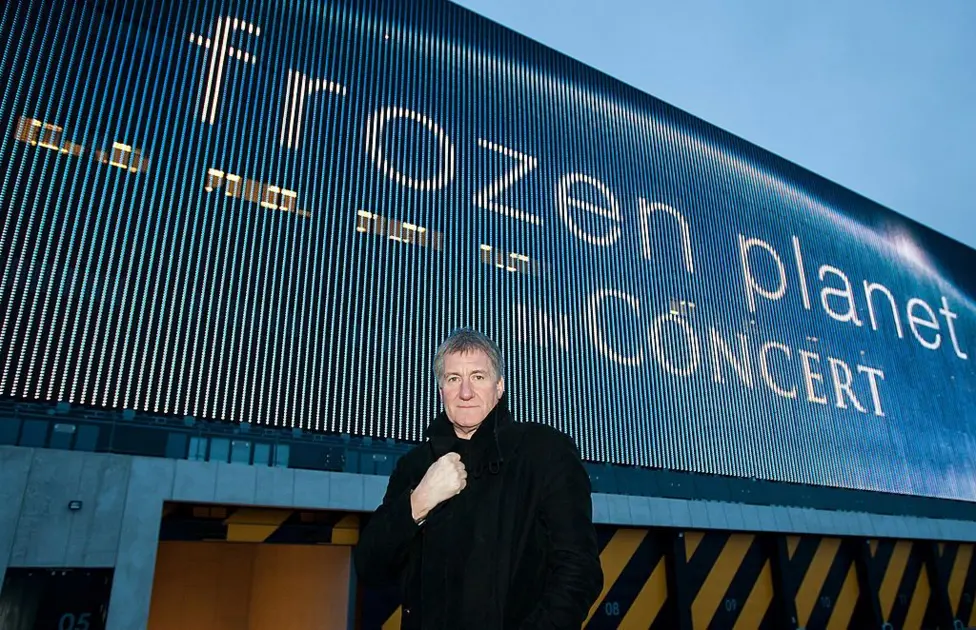 George Fenton stands next to a billboard promoting his orchestral show The Frozen Planet Live