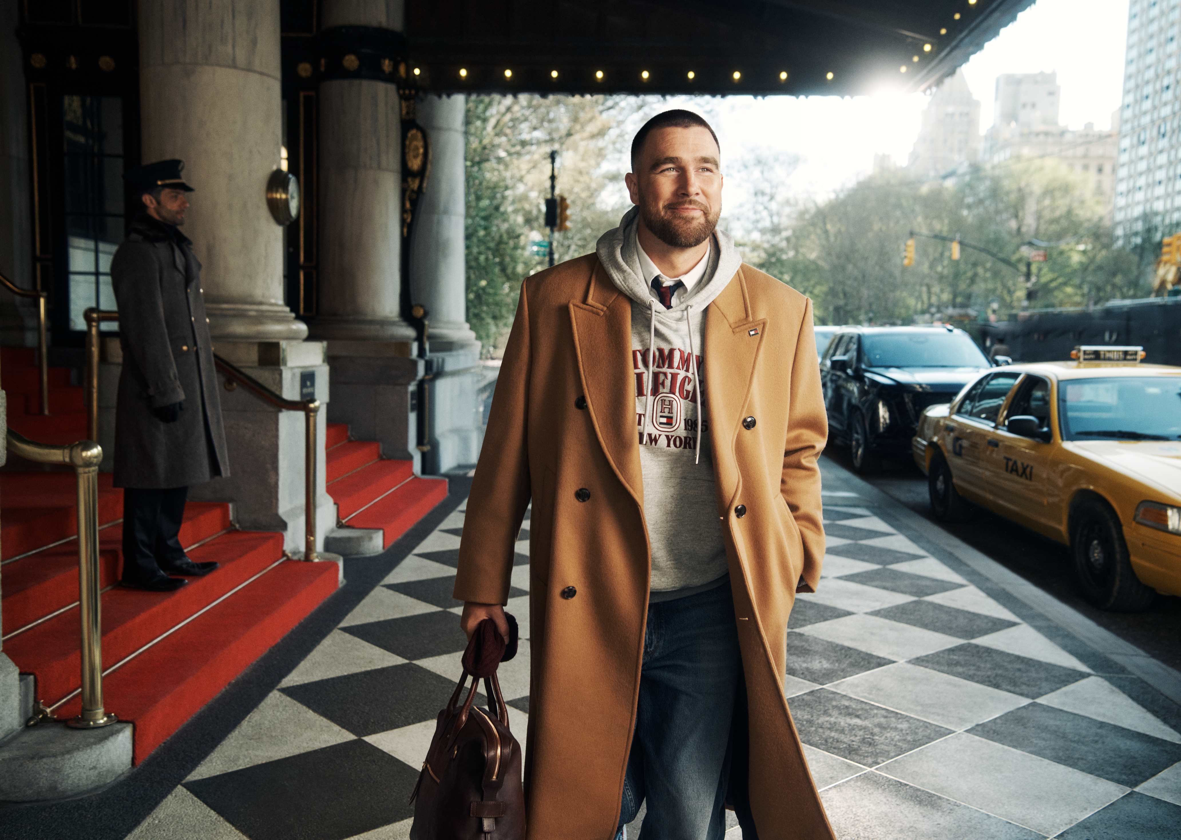 Travis Kelce in a Tommy Hilfiger campaign wearing a tan coat and a gray hoodie.