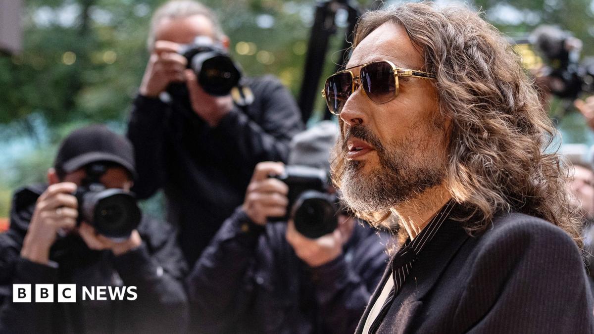 Russell Brand walking into court weraing sunglasses with three paparazzi photographers talking photos behind him