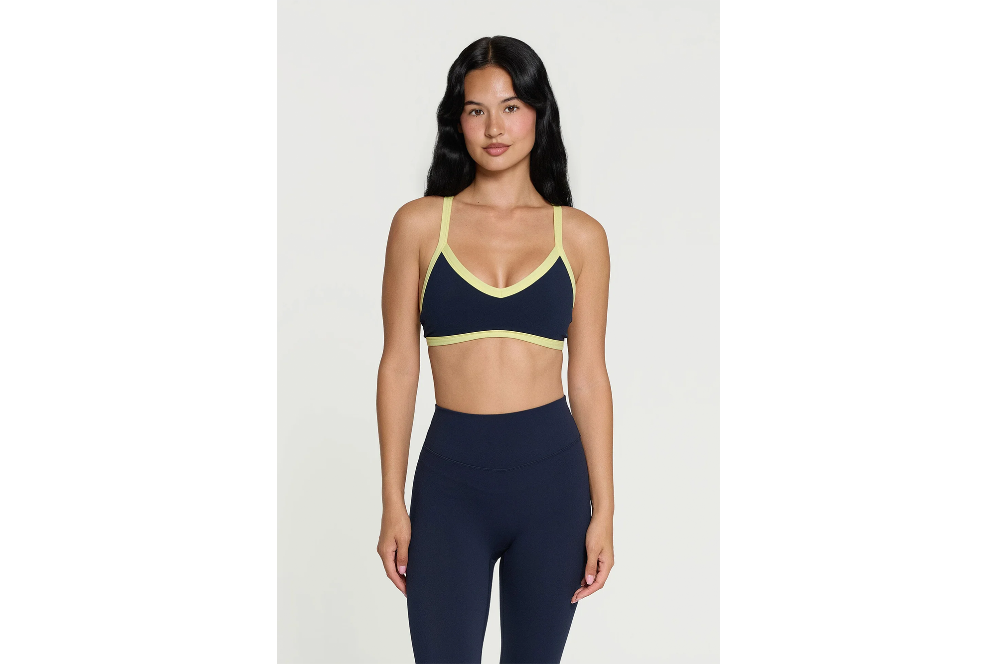 A woman models a navy blue sports bra with lime green trim and matching high-waisted leggings.