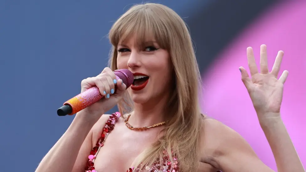 Taylor Swift waving while performing on stage at the Aviva Stadium in Dublin, during the Eras Tour in 2025