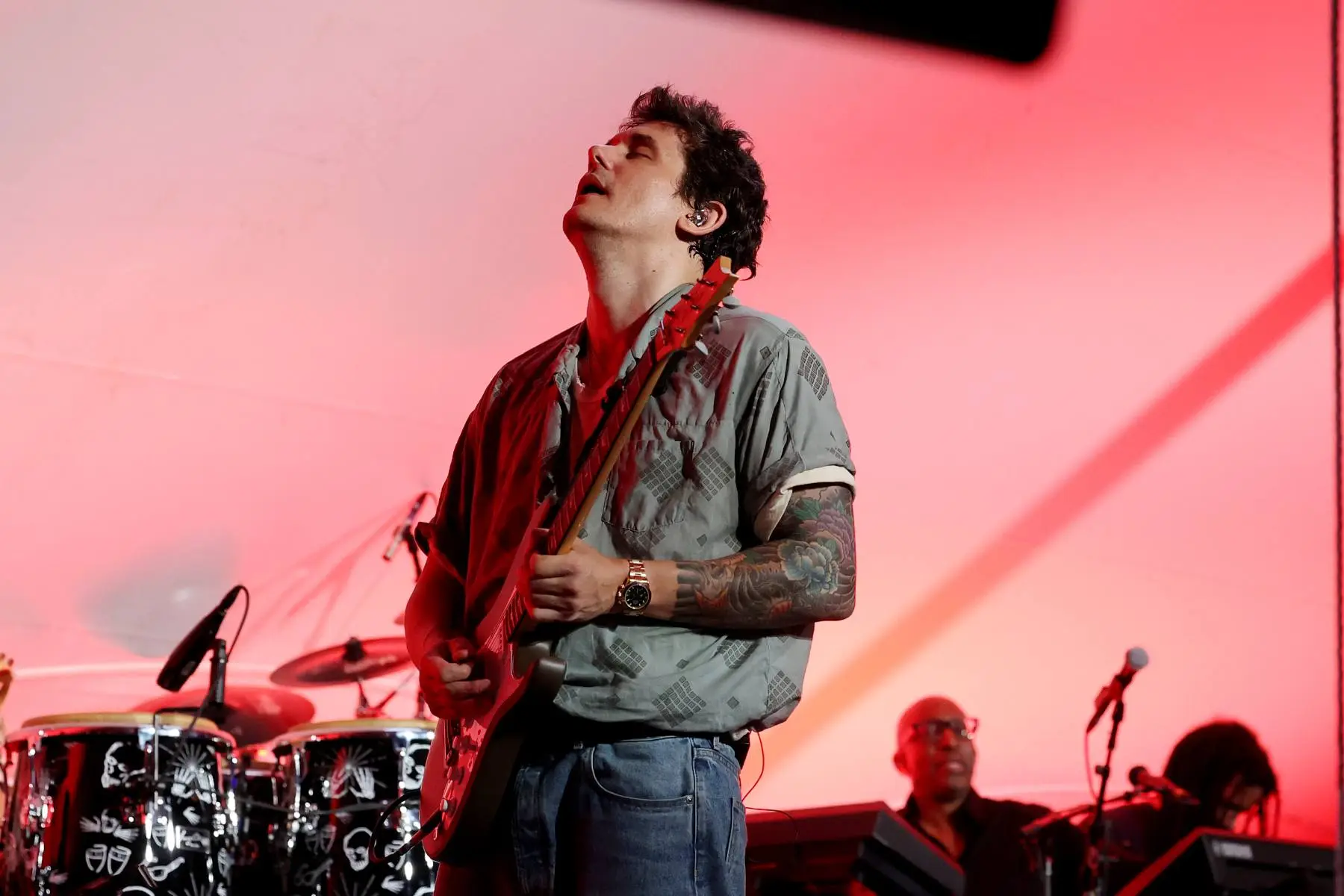 John Mayer performing live with an electric guitar under concert spotlights