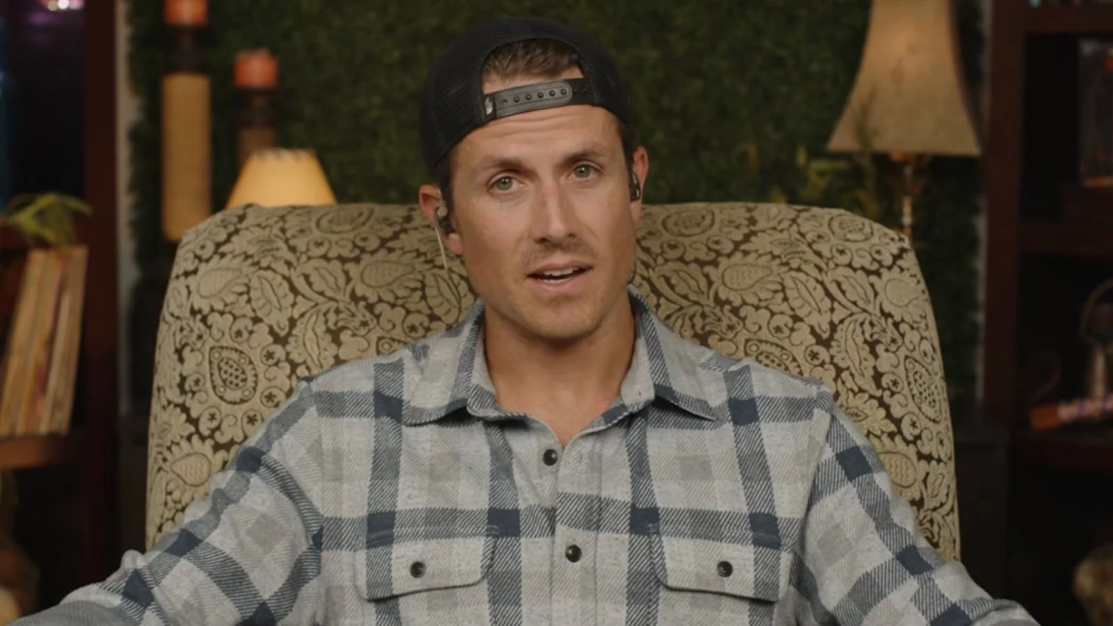 MrBallen sat in chequered shirt on chair in front of green background