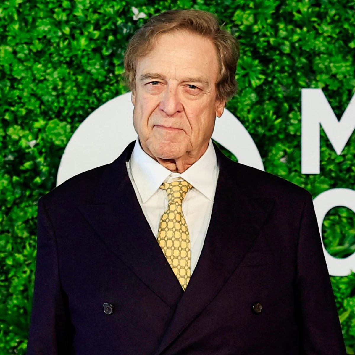 John Goodman posing on a red carpet showcasing his 200-pound weight loss transformation.