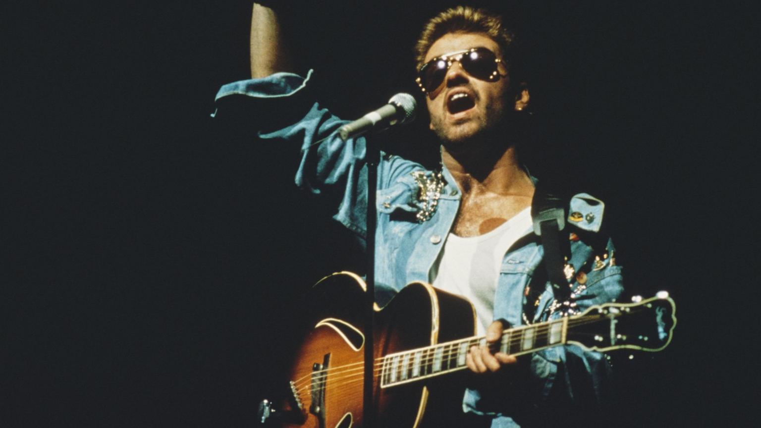 George Michael performing on stage with an acoustic guitar