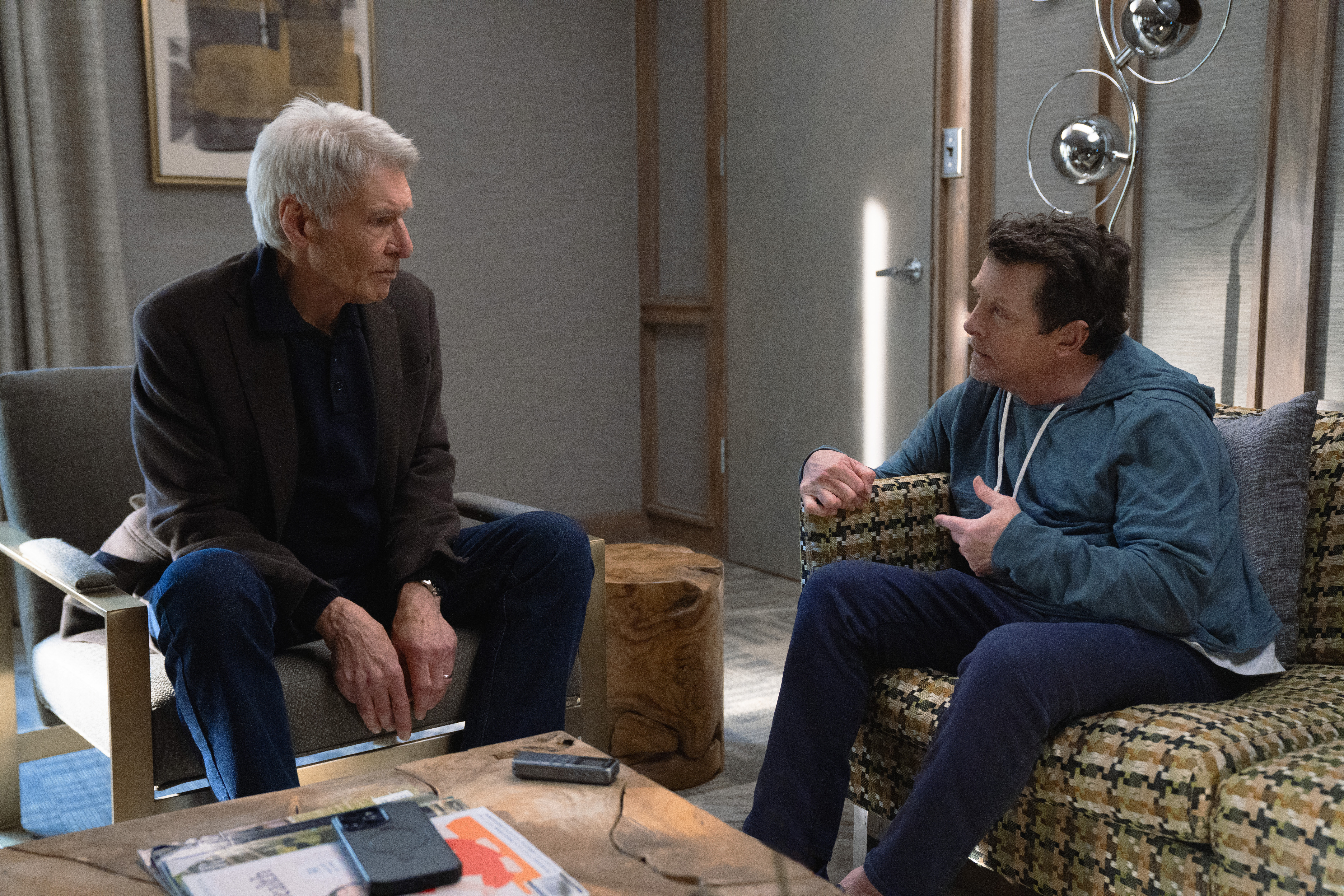 Michael J. Fox speaking to another man while seated in an episode of Shrinking.