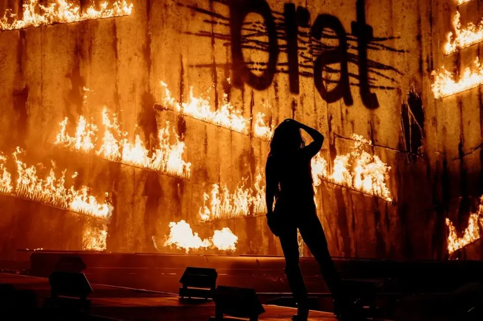 Charli XCX performing on stage at Glastonbury Festival 2025 in front of a firey backdrop and beneath a sign bearing the name of her biggest album, Brat