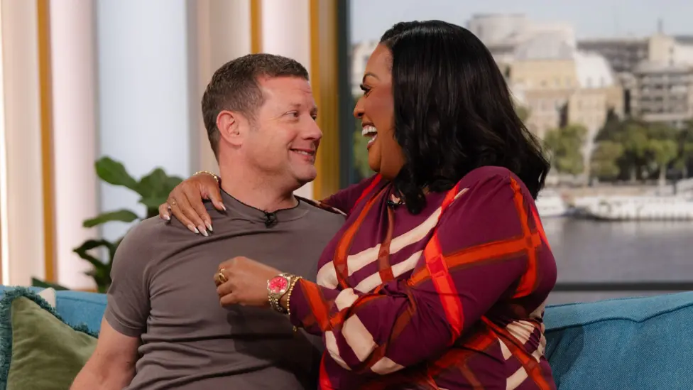 Alison Hammond laughing with an arm around Dermot O'Leary, who is smiling nervously, on the set of This Morning