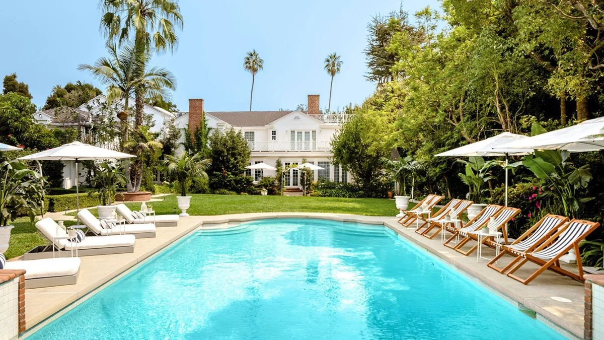 Outside of white mansion with blue pool and deck chairs