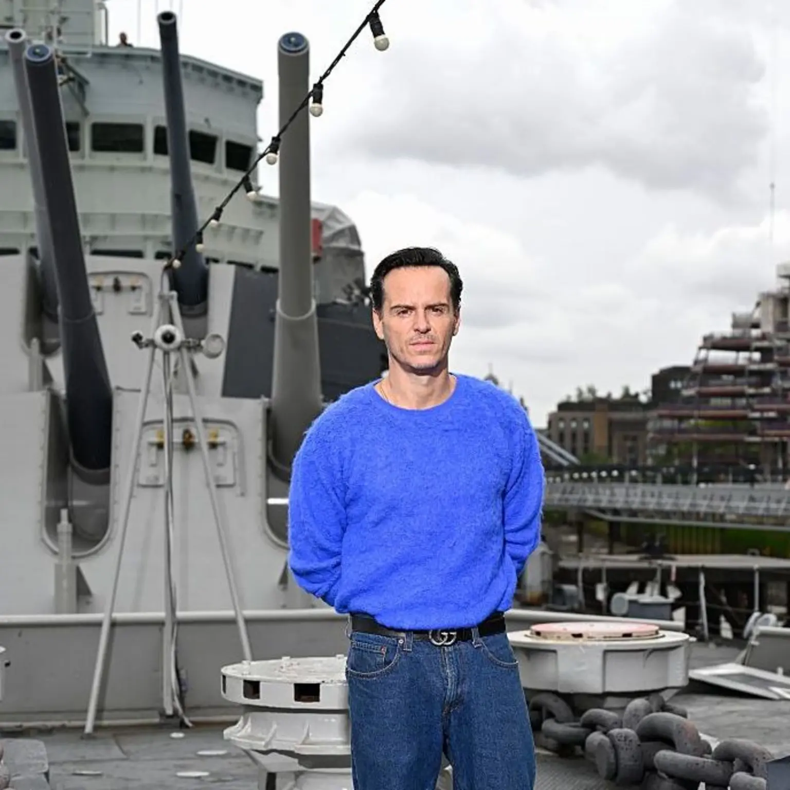 Andrew Scott in a blue jumper and jeans on HMS Belfast