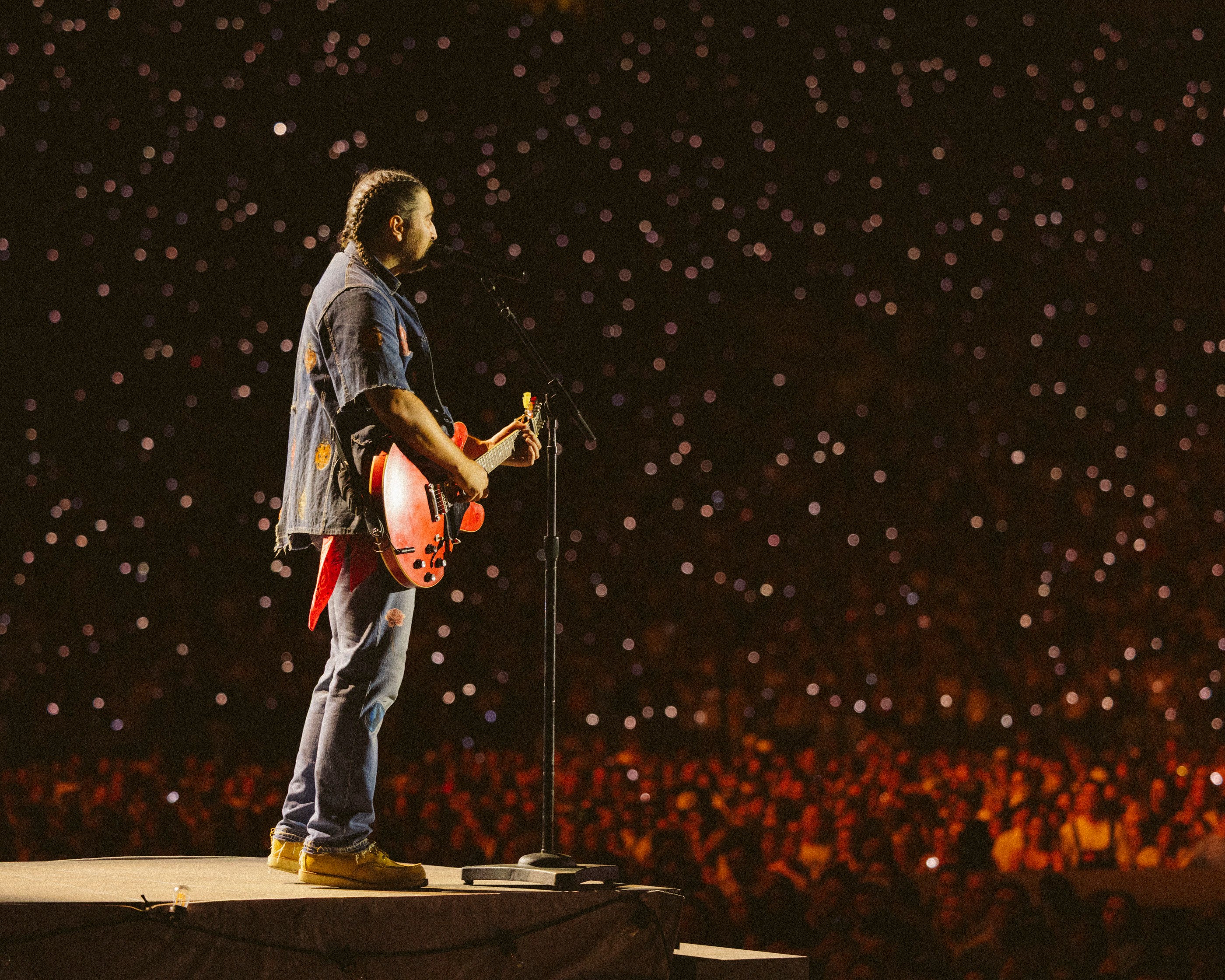 Noah Kahan performing on stage at the Rose Bowl Stadium during a concert.
