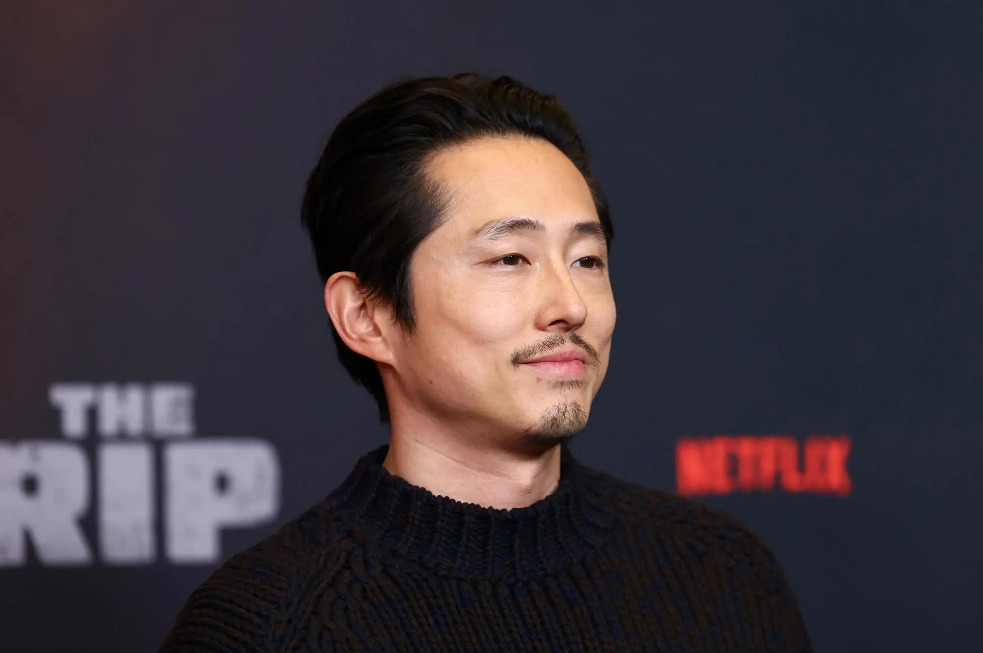 Steven Yeun posing on a red carpet in a black suit