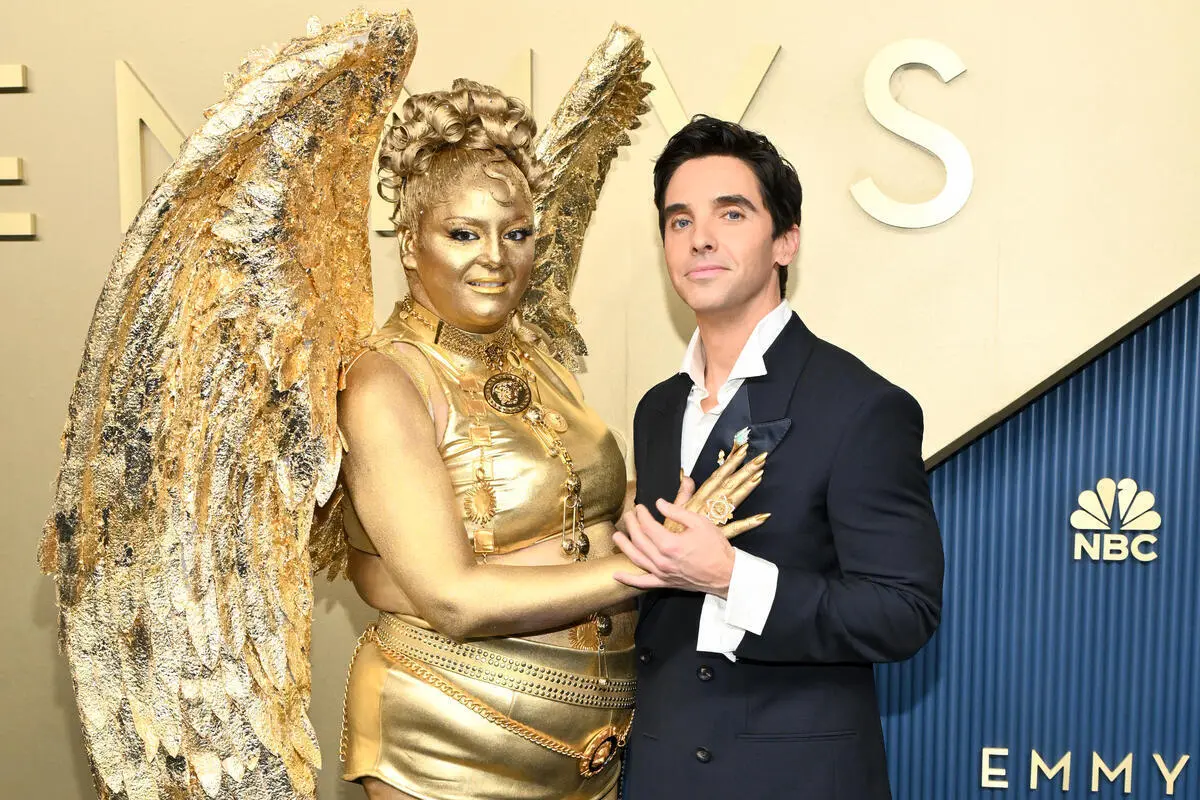 Meg Stalter dressed as a gold Emmy award statue on the red carpet alongside Paul W. Downs