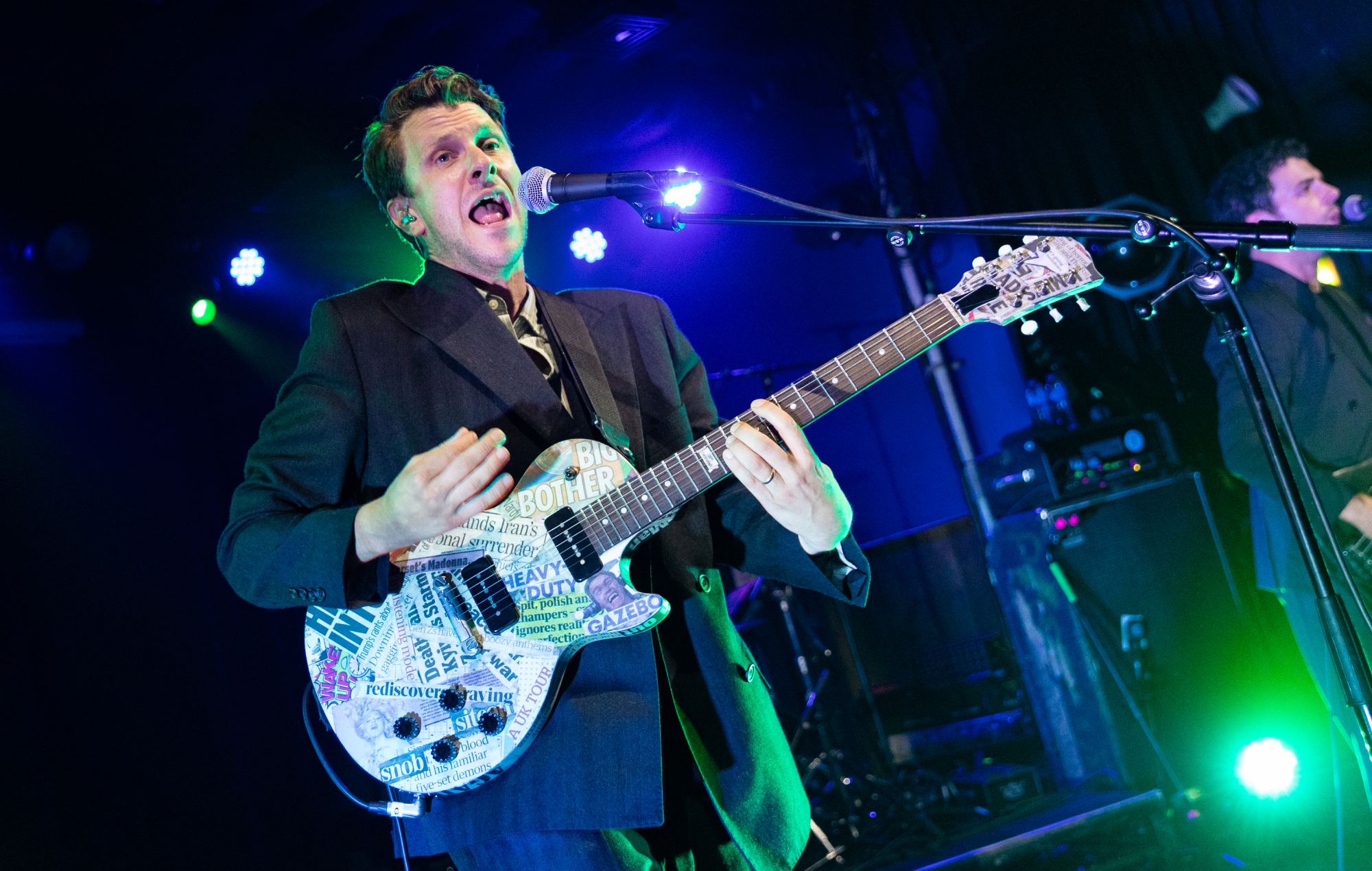 Jamie T holding a mic and performing live on stage in front of a glowing venue crowd