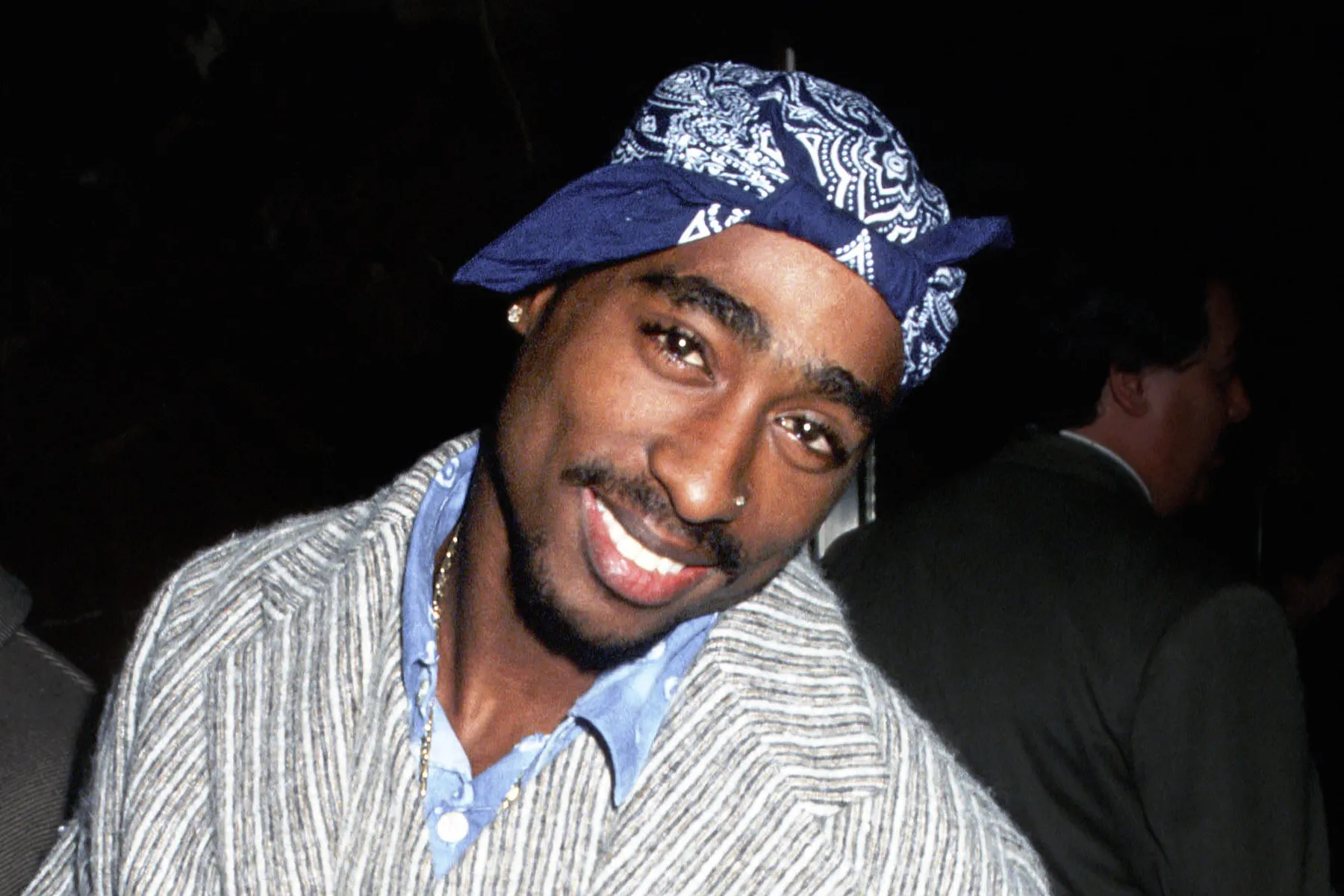 Tupac Shakur wearing his iconic bandana and smiling at a public event in the 1990s