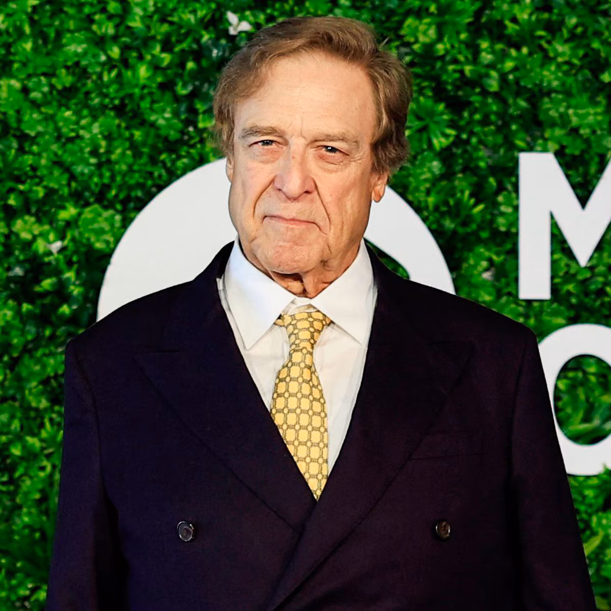 John Goodman posing on a red carpet showcasing his 200-pound weight loss transformation.