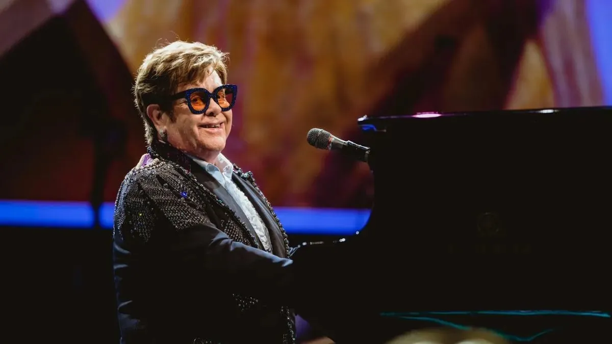 Elton John performing live at a grand piano during a stadium concert set