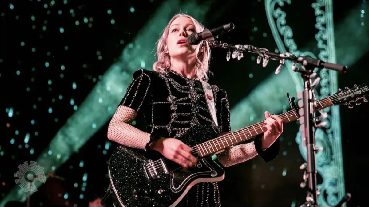 Phoebe Bridgers performing on stage with her guitar.