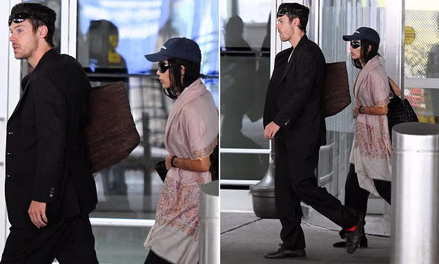 Harry Styles walking in a black suit after landing at JFK Airport in New York City with Zoe Kravitz.