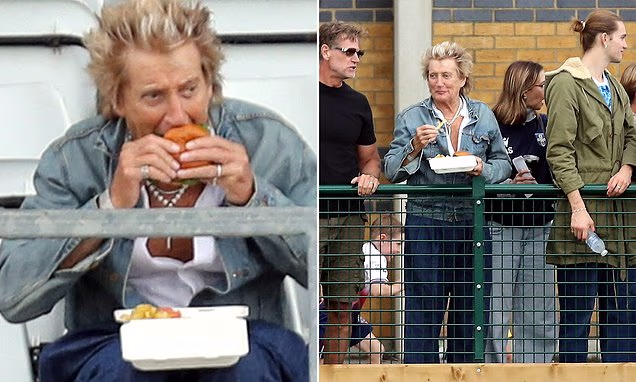 Sir Rod Stewart sitting in the stands eating a burger next to his son Alastair at a football game