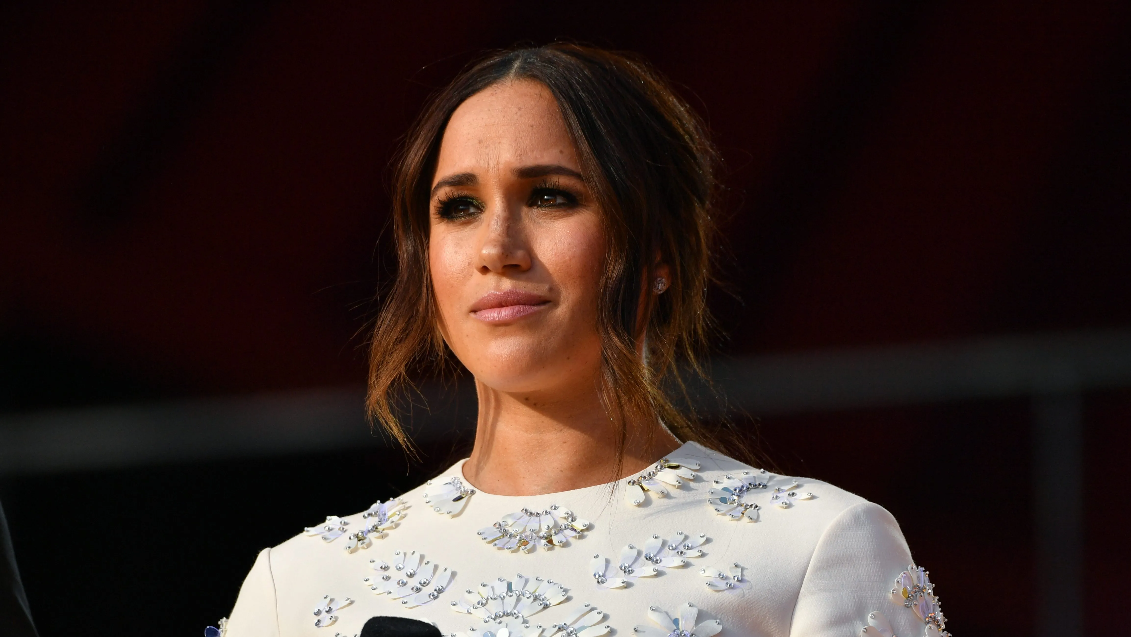 Meghan Markle smiling at a red carpet media event in a chic neutral ensemble.