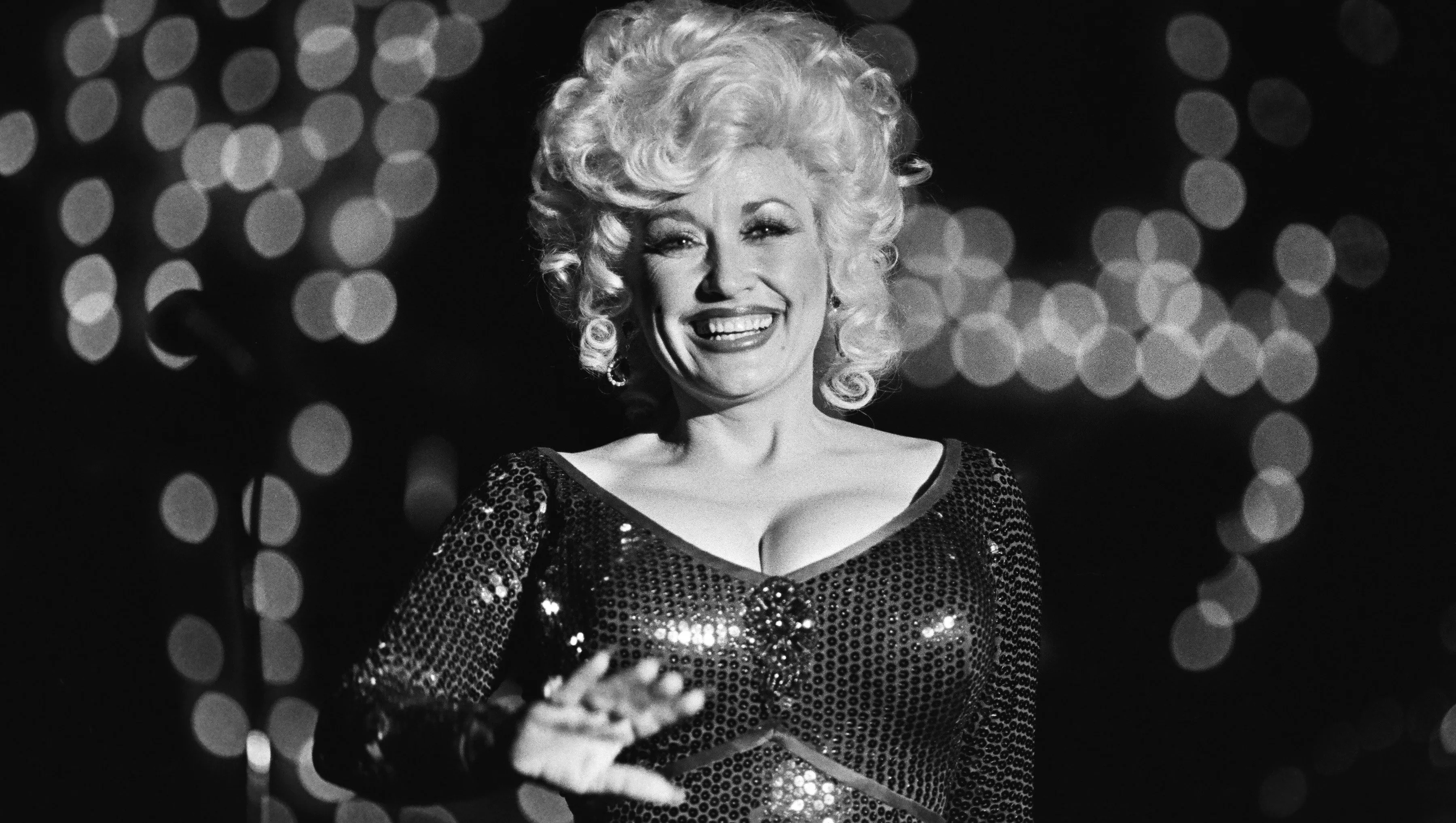 Dolly Parton smiling at a red carpet event in a sparkly outfit