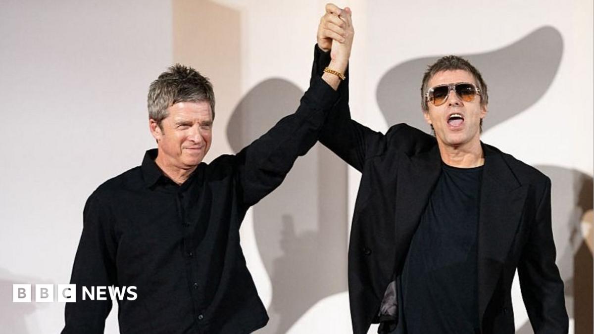 The Gallagher brothers hand in hand, raising the arms. They are both in black suits