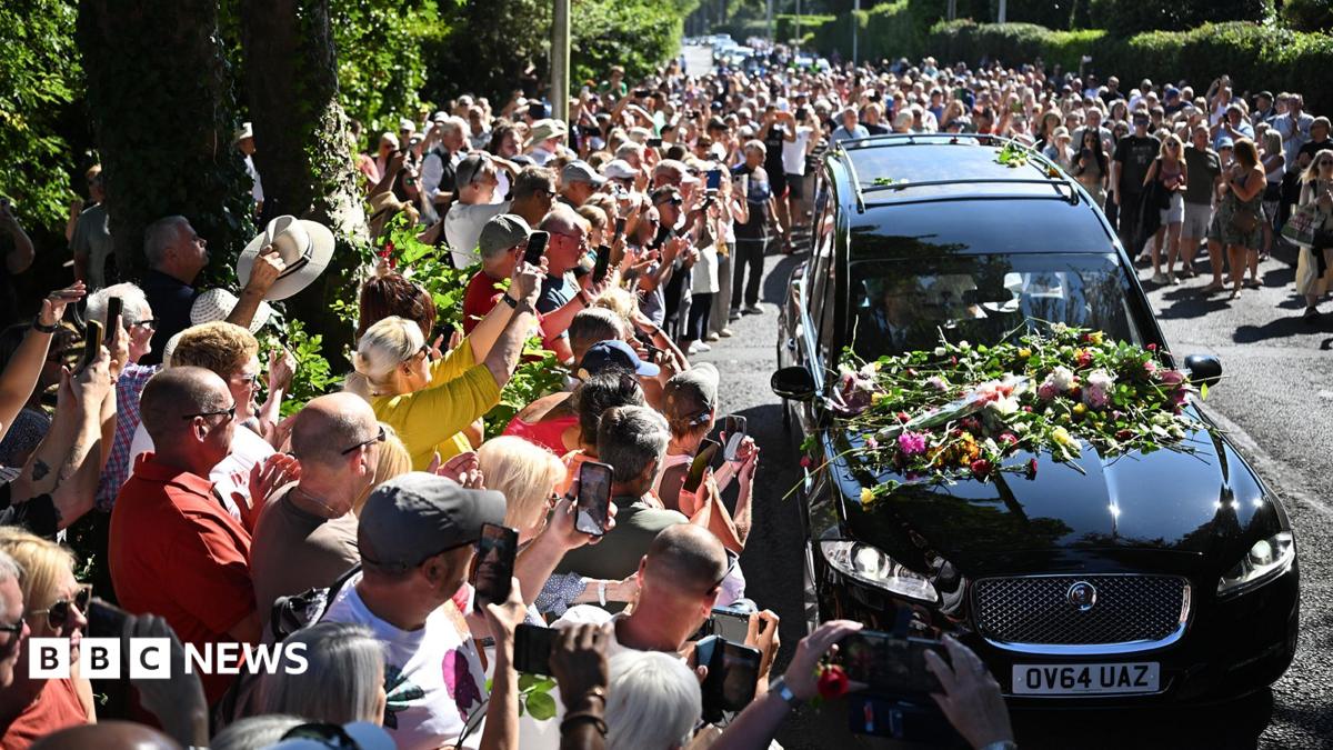 Bystanders flock towards a black hearse and throw flowers onto its bonnet as it drives through the town carrying the coffin of Bonnie Tyler.