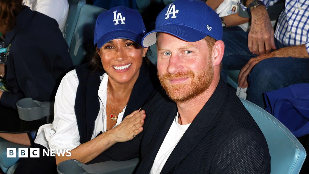 Meghan and Harry in blue baseball caps watching a game at the Dodgers Stadium in Los Angeles
