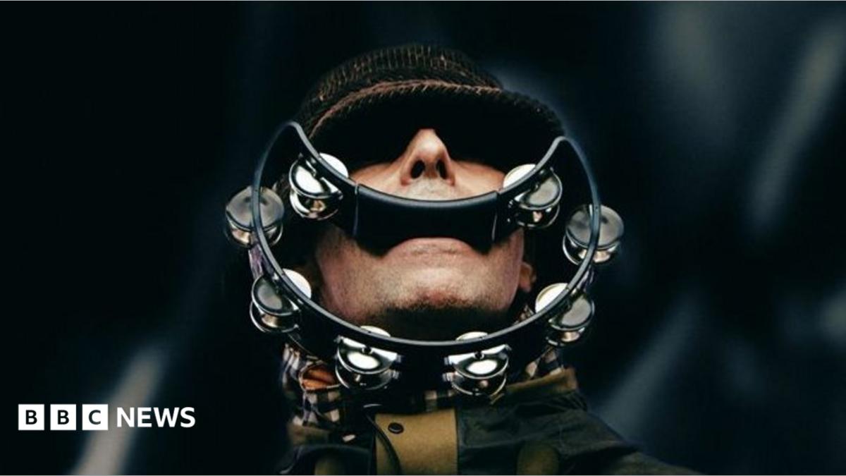 Liam Gallagher of Oasis with his eyes shaded by the peak of his hat, with a smile-shaped tambourine in his mouth