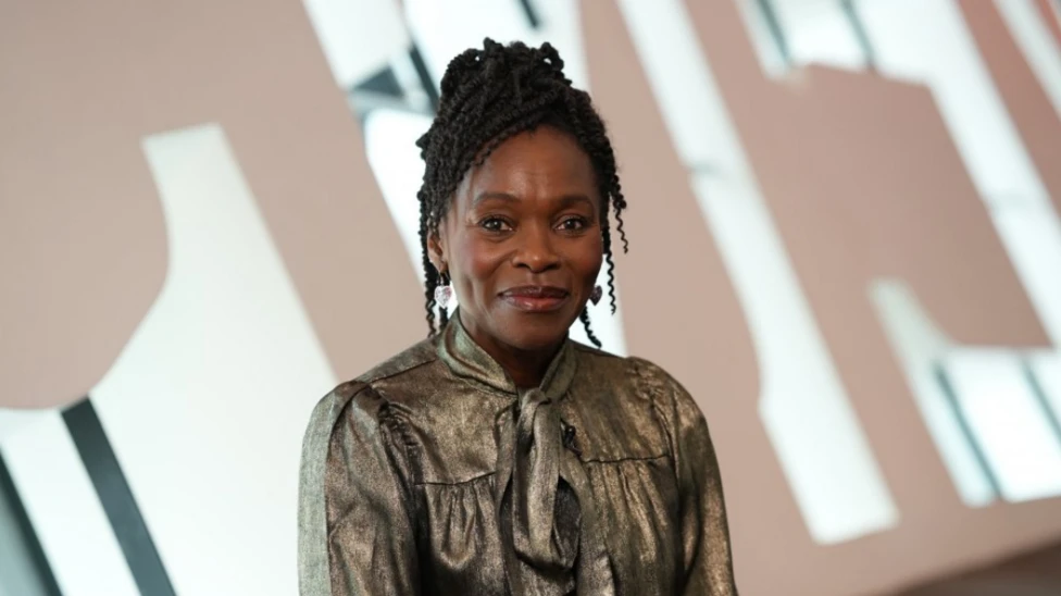 Rakie Ayola smiles towards the camera wearing a metallic top. She is sitting in front of the Wales Millennium Centre letters indoors