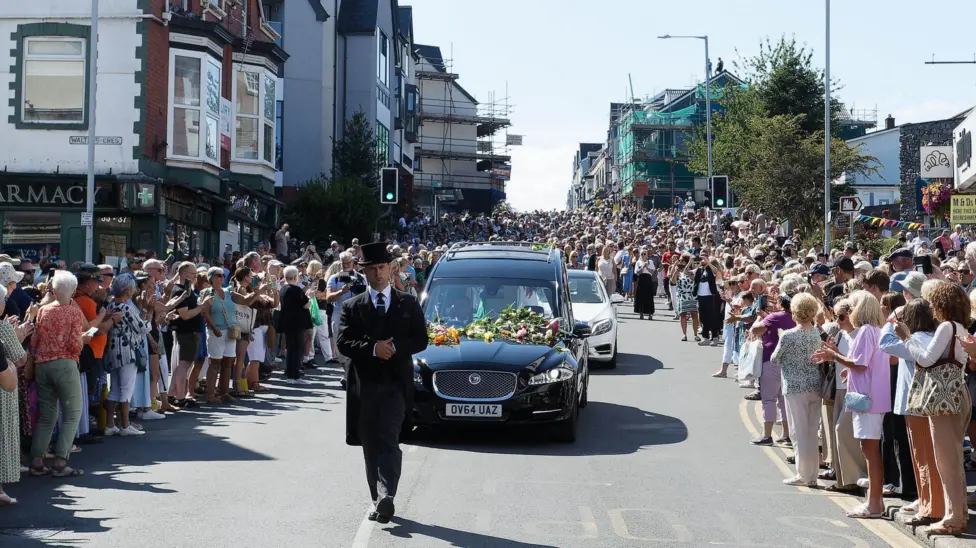 Thousands of fans gathered in the street as Bonnie Tyler's coffin drives down the road in a black funeral car.