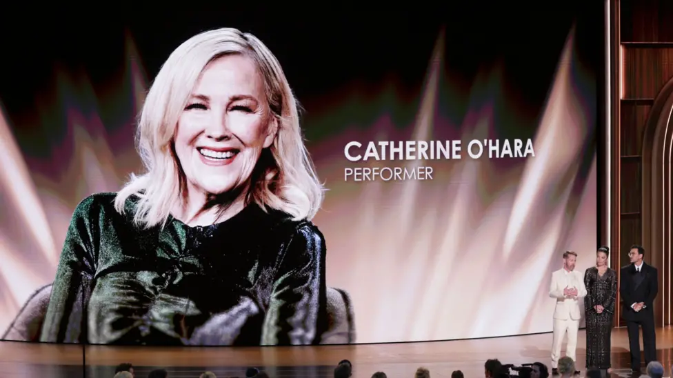 Macaulay Culkin, Annie Murphy and Dan Levy speak onstage next to a big backdrop honouring Catherine O'Hara at the Emmys