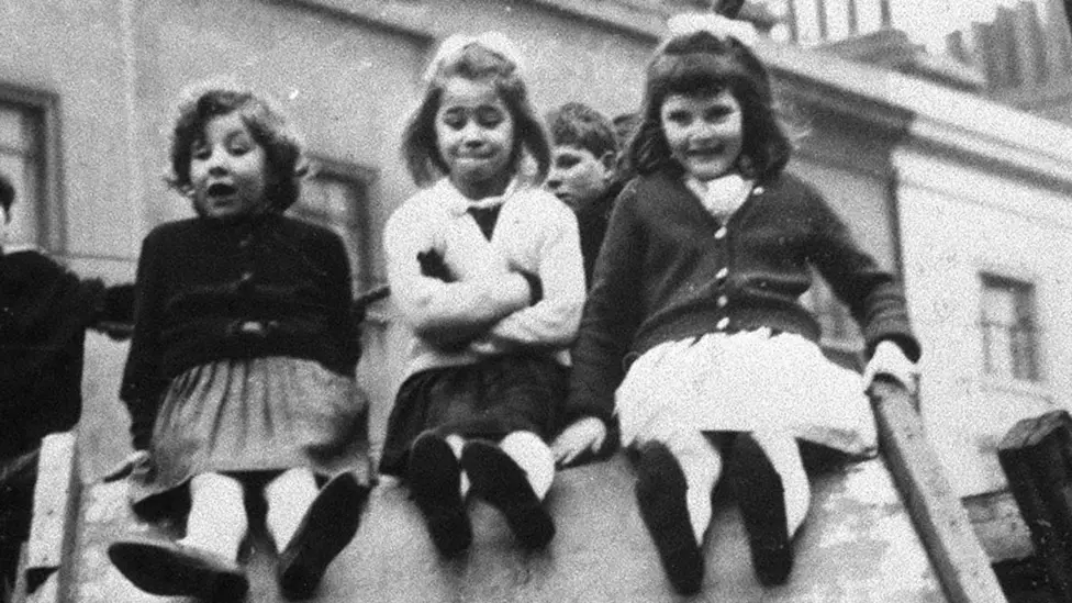 Jackie, far left, sits at the top of a slide in a children's playground in east London in 7 Up with Lynn and Sue.