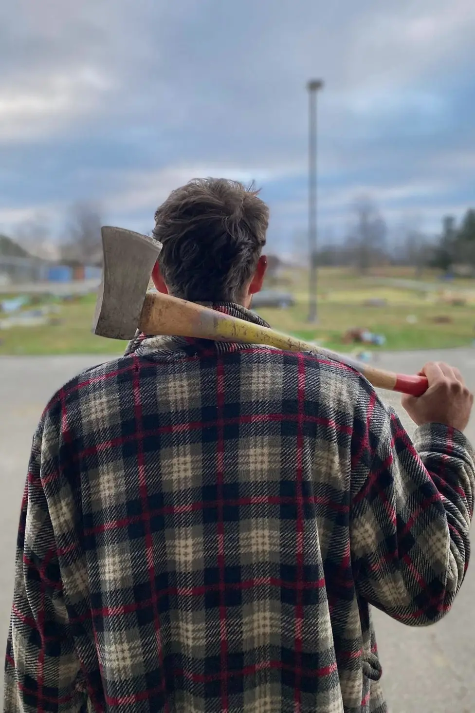 Ioan Humphreys facing away from the camera. He is wearing a tartan jacket and holding an axe over his right shoudler.