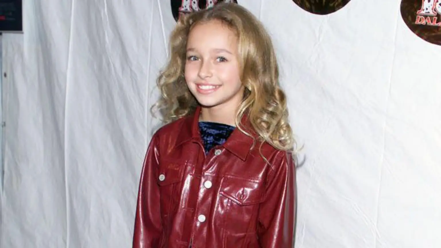 Panettiere pictured smiling at 11-years-old at a film premiere. She has curly dark blonde hair and wears a vinyl dark red jacket with a crused velvet blue top.
