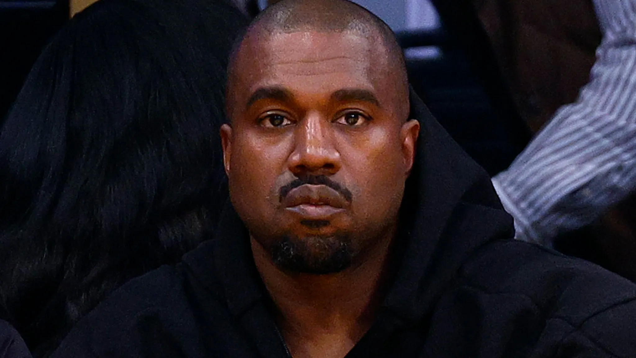 Kanye West wearing a black hooded jacket looking serious at an event