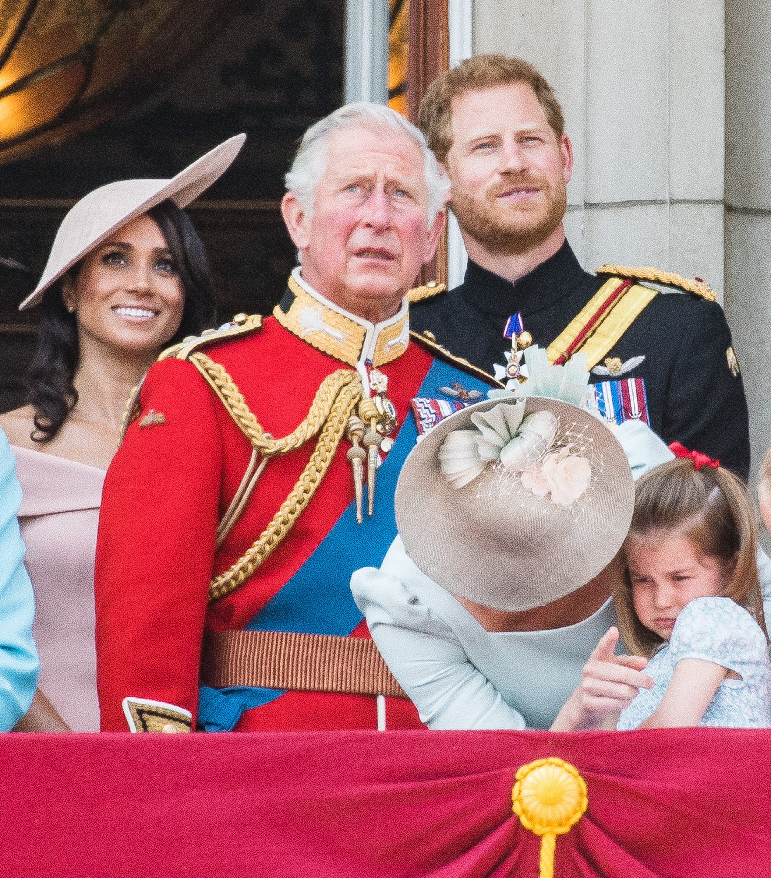 Meghan, Duchess of Sussex, in an off-shoulder pink dress and pink hat, King Charles, in a red military jacket, blue sash and medals, Prince Harry, Duke of Sussex, in a black military jacket and medals, Catherine, Duchess