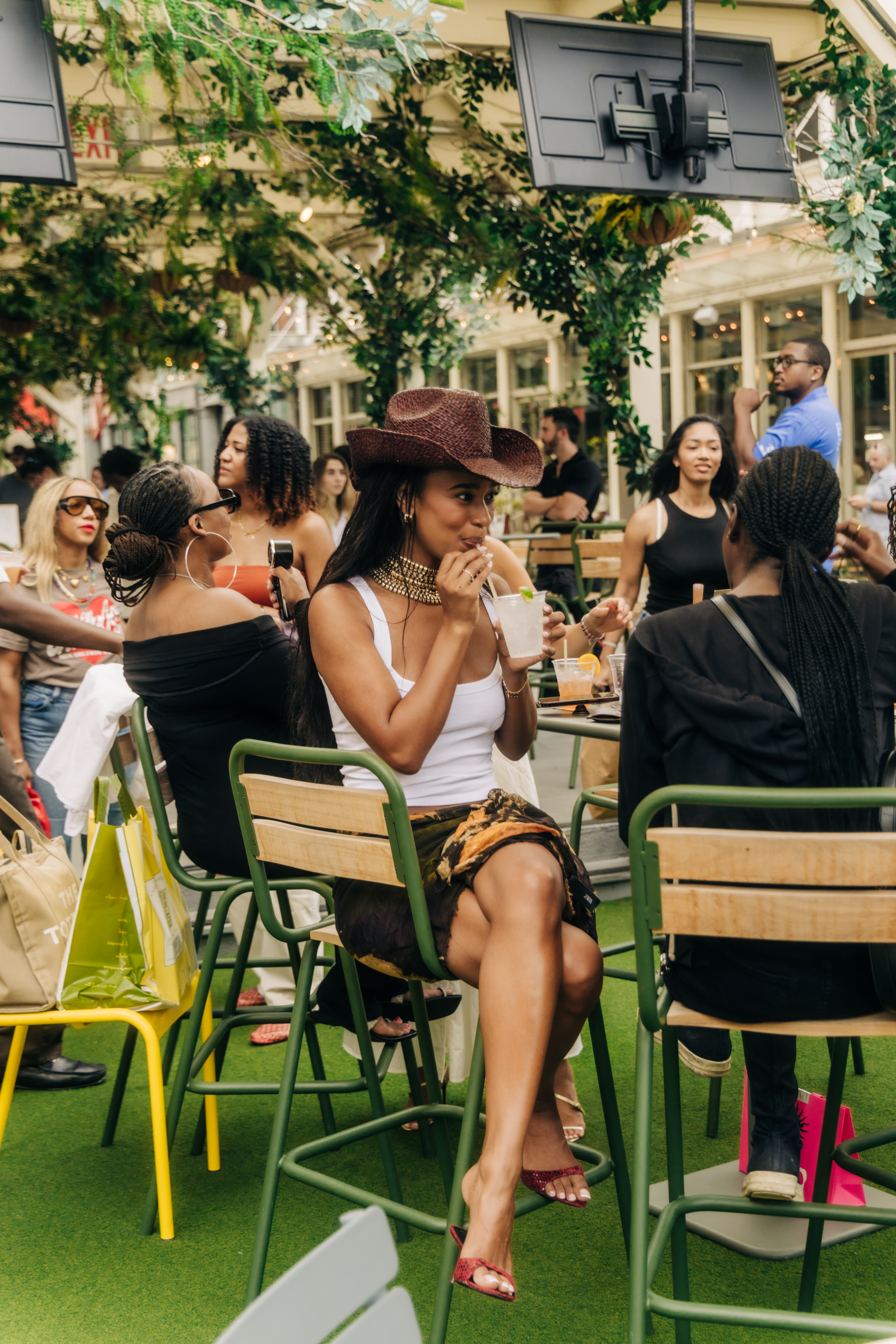 Mia Calabrese wearing a straw hat and gold necklace, sipping a drink at Sadie