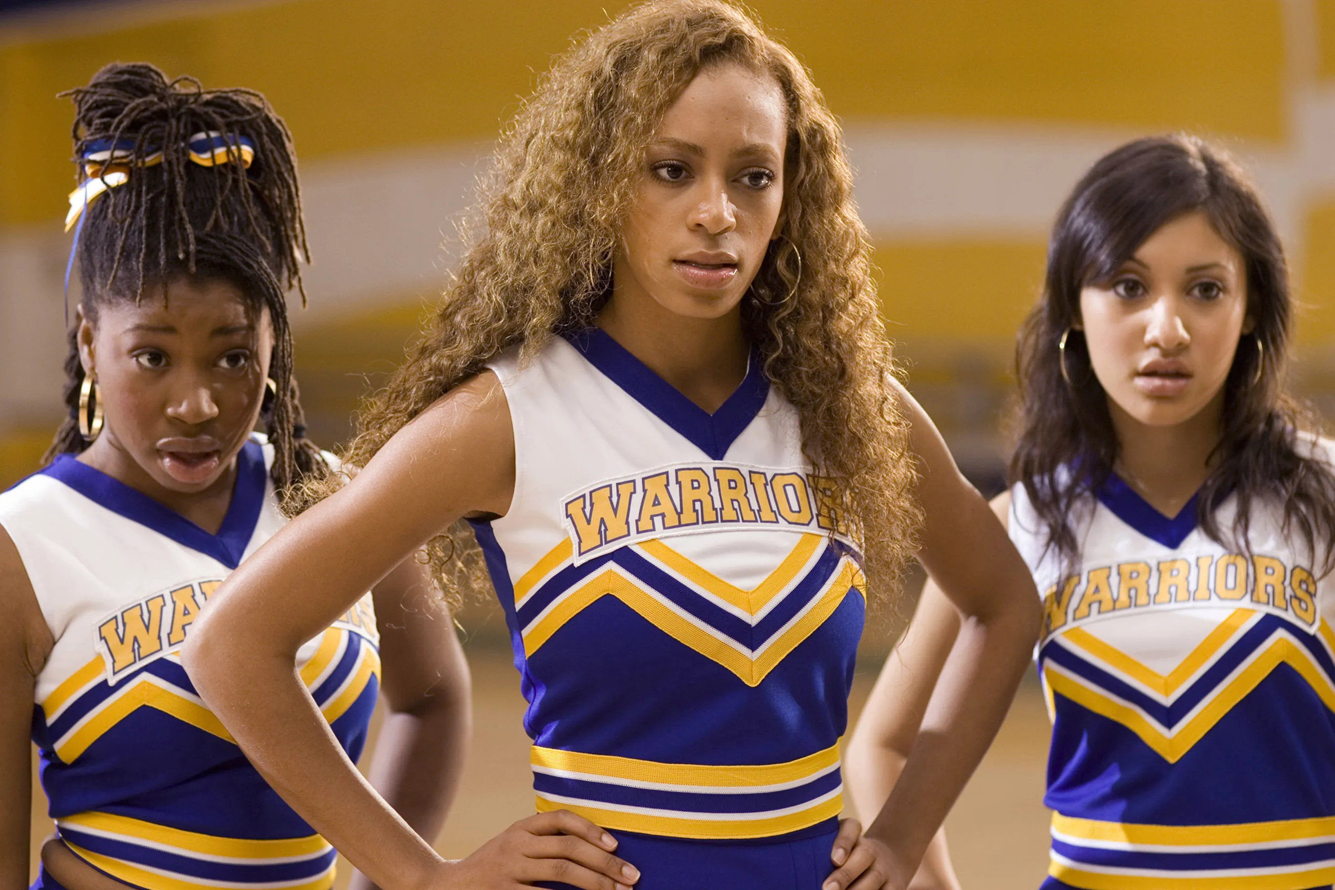 Three cheerleaders in "Warriors" uniforms with hands on hips.