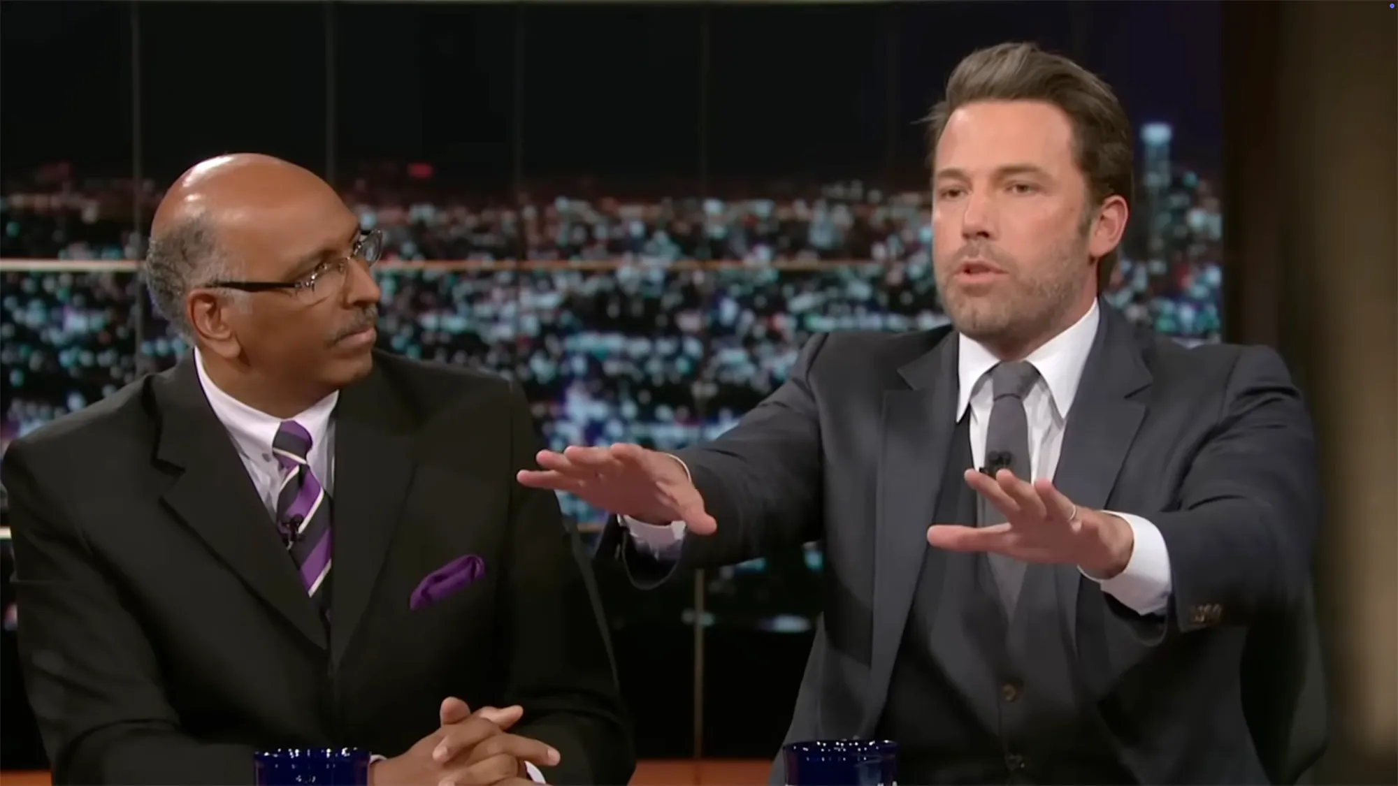 Ben Affleck speaking passionately while gesturing with his hands next to a man in glasses looking intently at him.