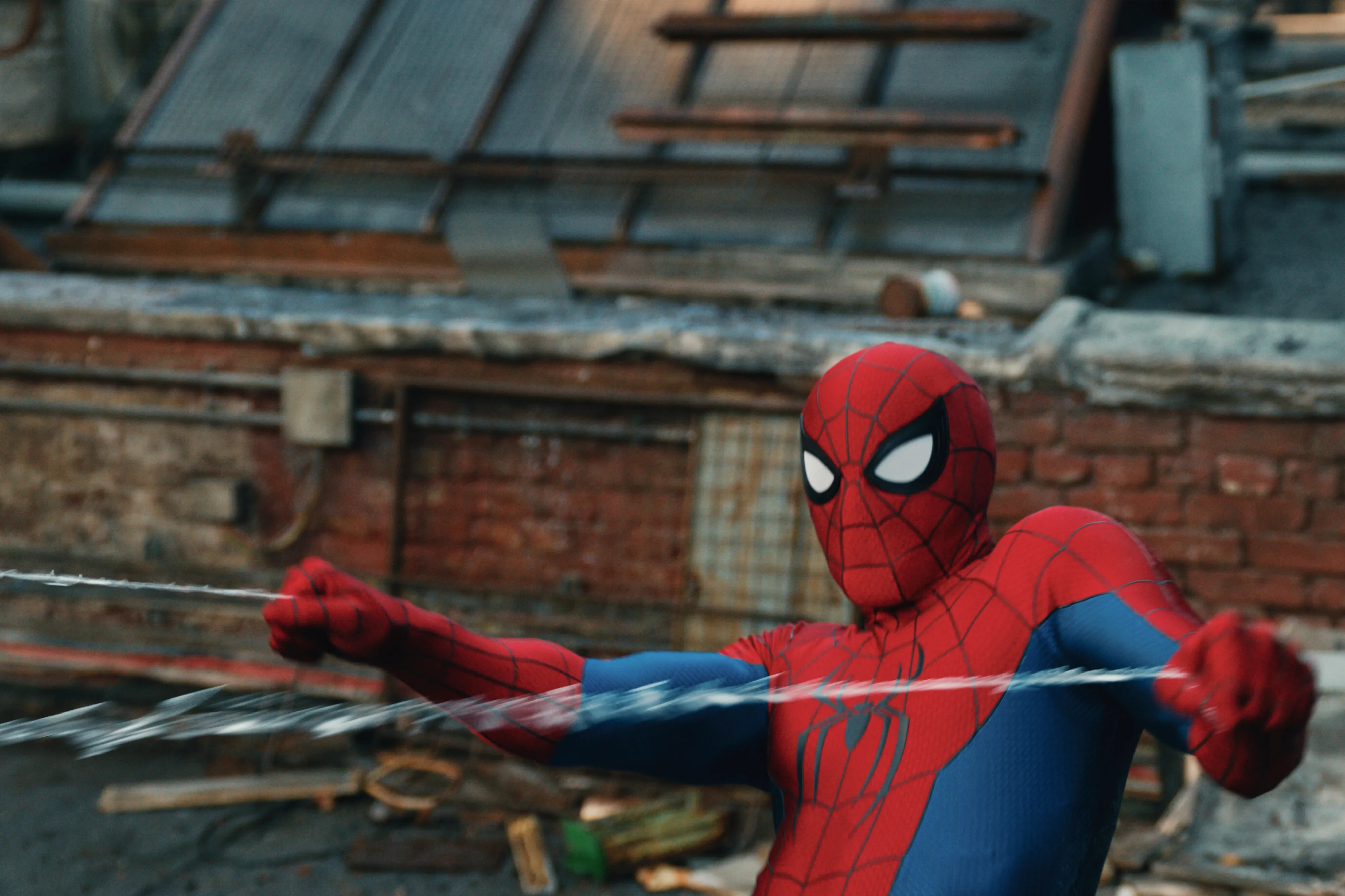 Spider-Man swinging with a web, against a brick building.