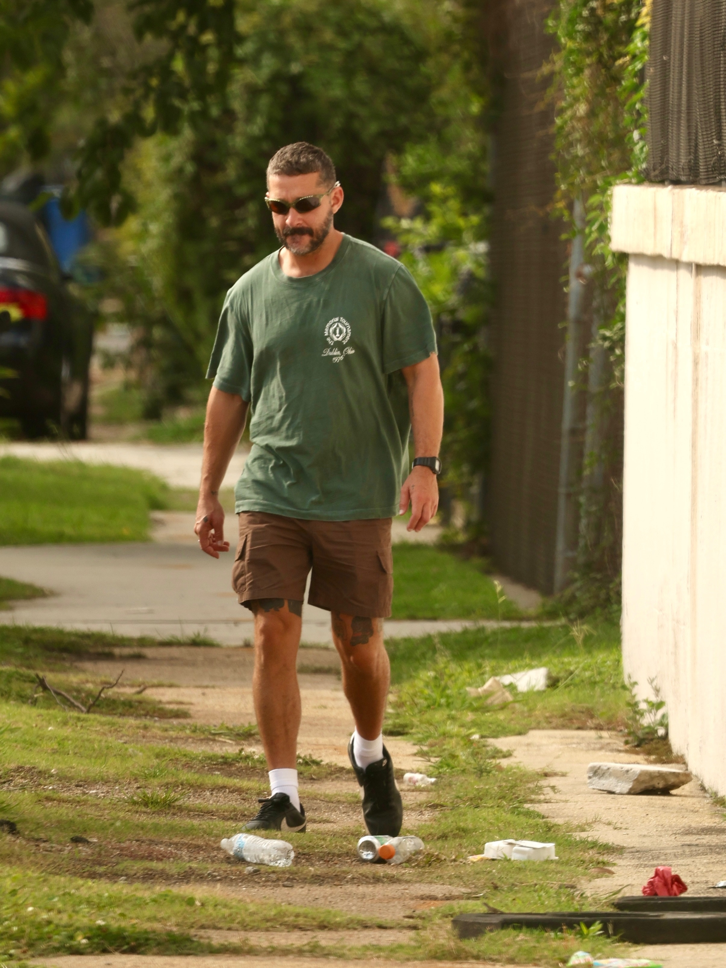 Shia LaBeouf walking down a grassy sidewalk in New Orleans.