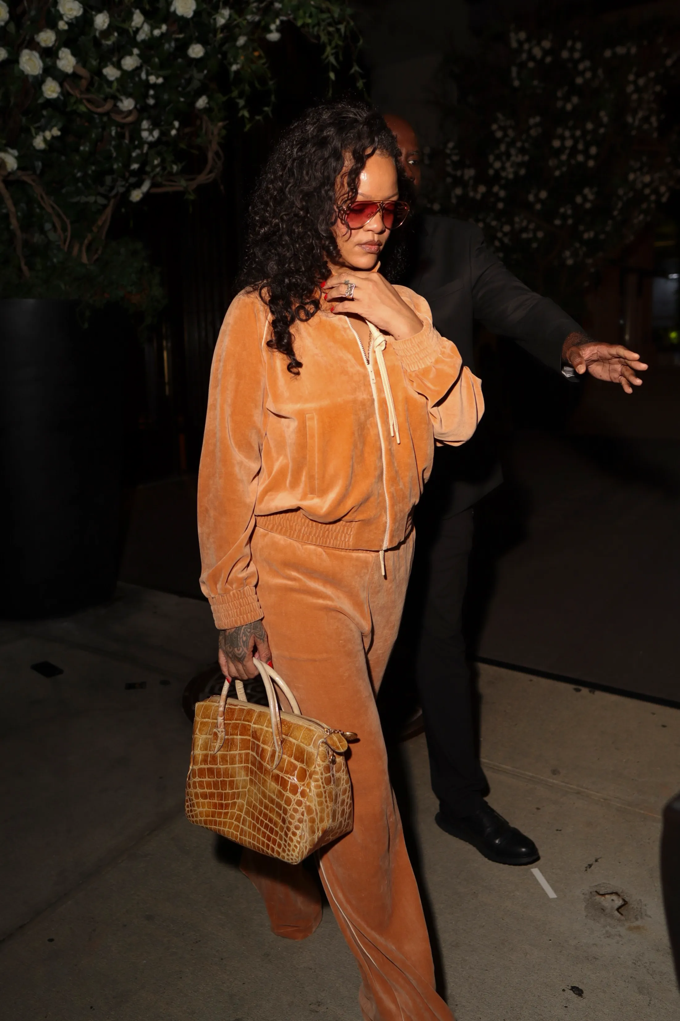 Rihanna in an orange velvet outfit, red sunglasses, and a crocodile-skin handbag.