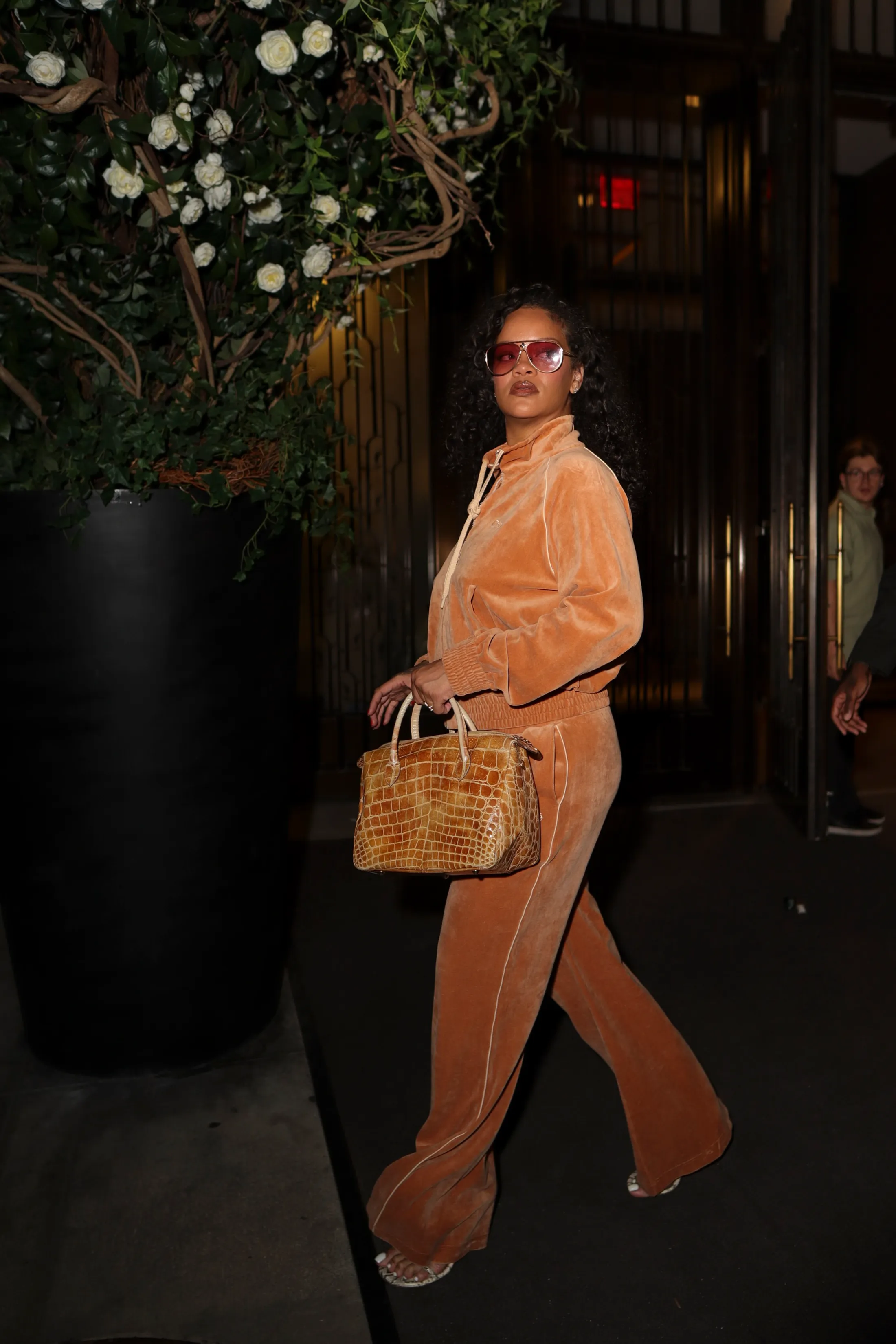Rihanna in an orange velvet outfit, red sunglasses, and a snakeskin handbag, leaving her New York City hotel.