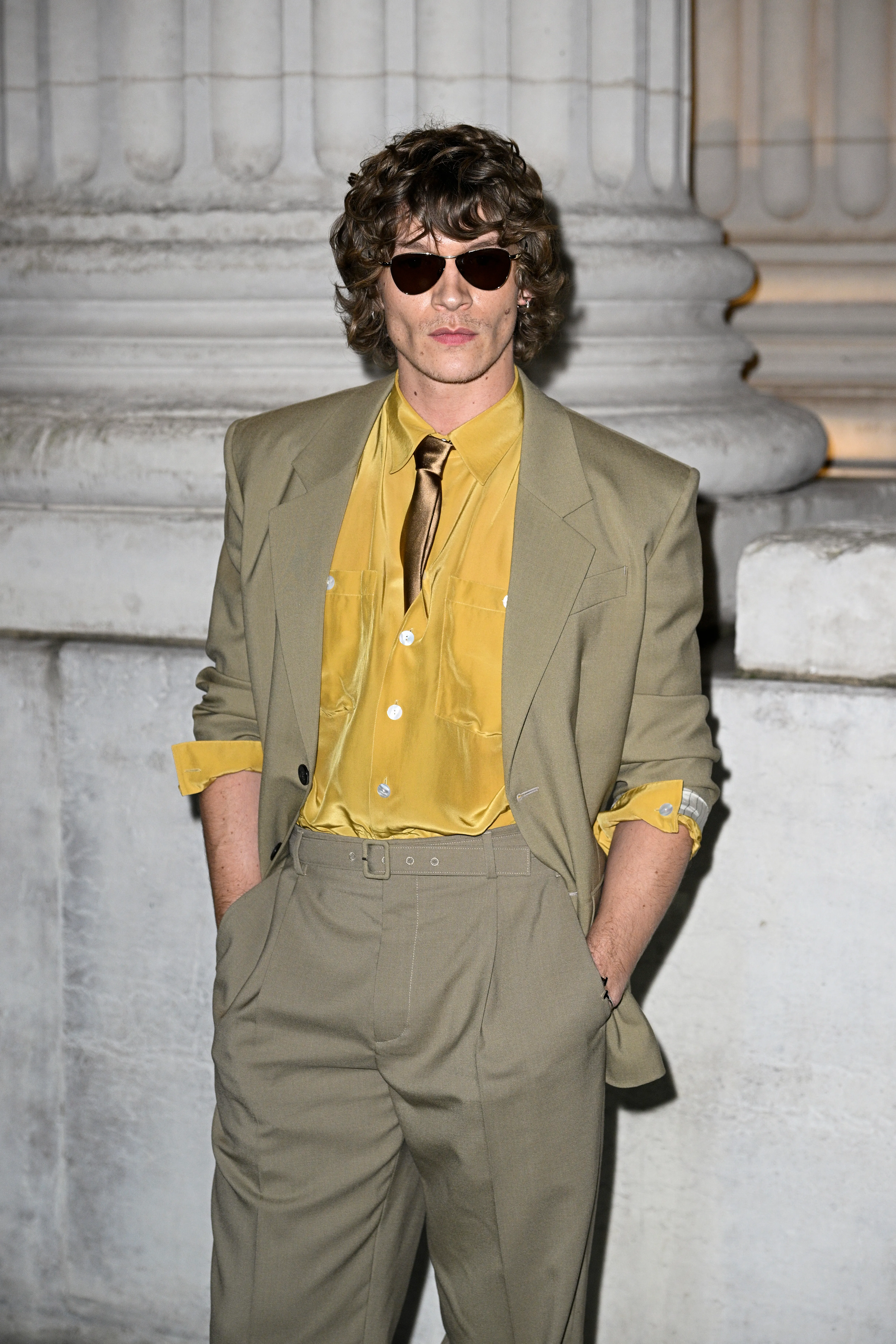 Connor Storrie at Paris Fashion Week in a beige suit, mustard shirt, and sunglasses.
