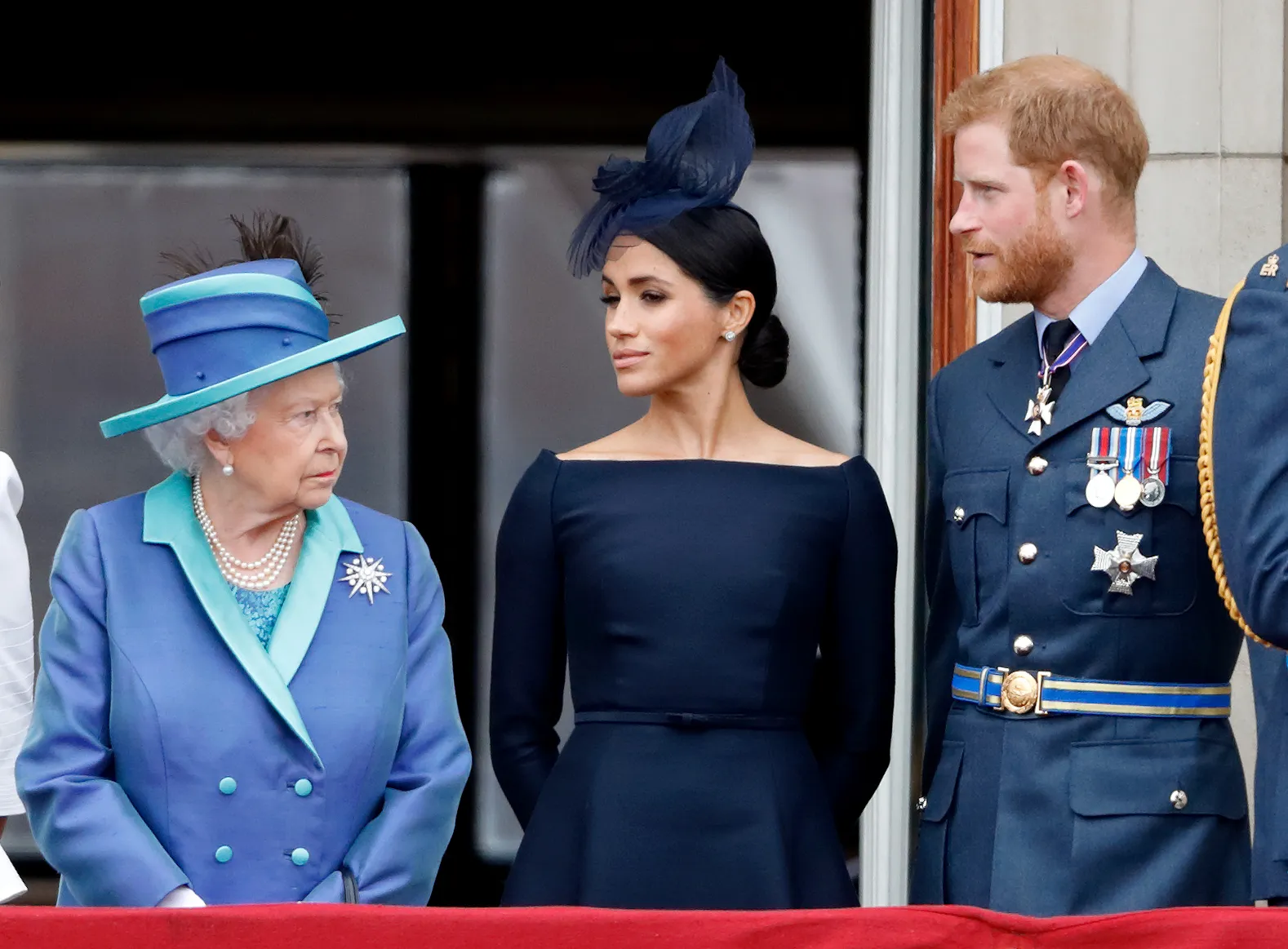 Queen Elizabeth II, in a blue coat with turquoise trim and matching hat, Meghan, Duchess of Sussex, in a navy blue dress and blue hat, and Prince Harry, Duke of Sussex, in a blue military jacket and medals, watch a flypa